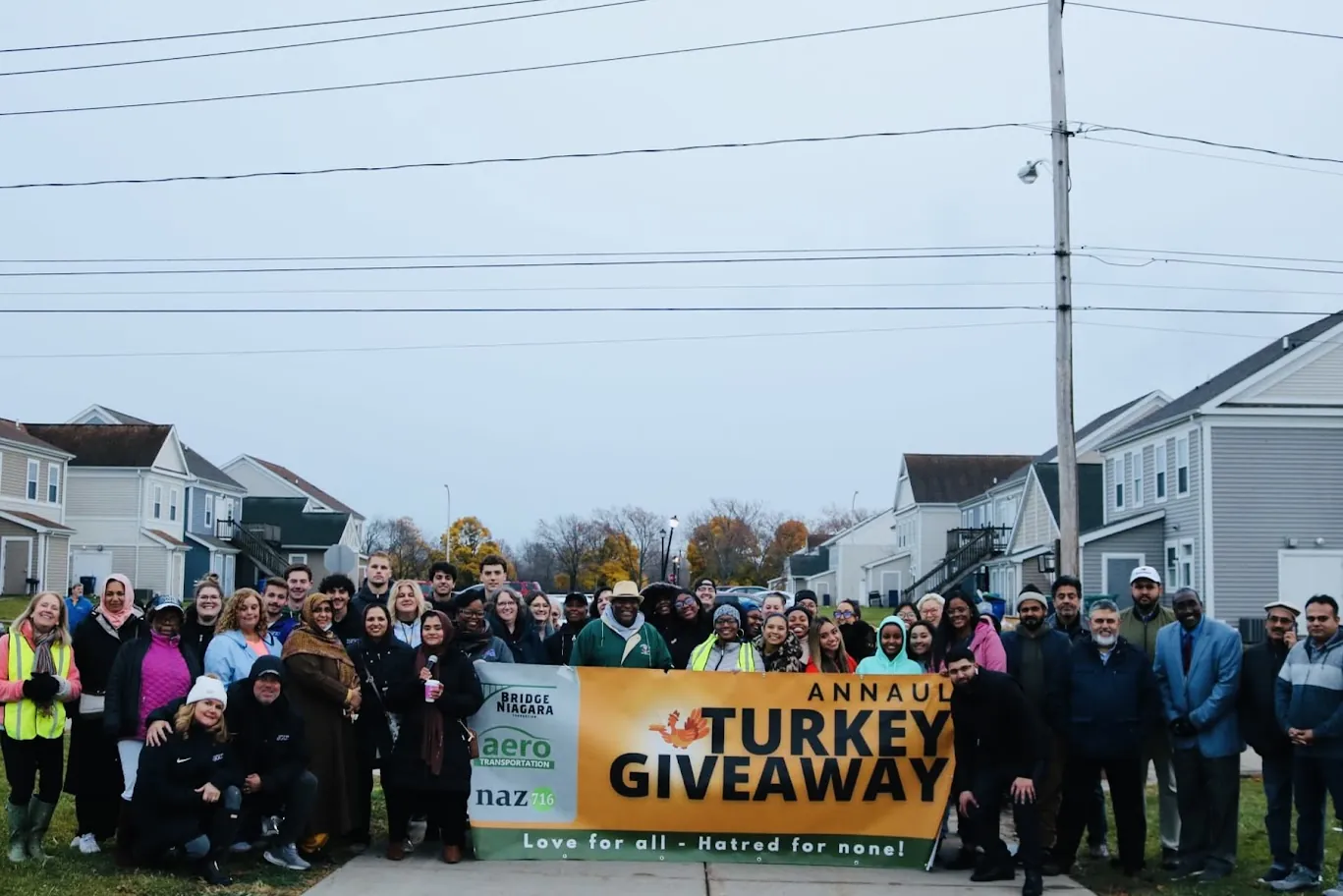 A large group of community members and volunteers gathers behind a Turkey Giveaway banner at a past event